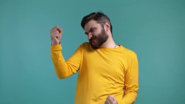 İnsanoğlu çok mutlu ve mutlu, zaferin evet jestini gösteriyor, başarıya ulaşıyor, hedeflere ulaşılıyor. Mavi arka planda heyecanlı, şanslı sakallı adam. Büyük ikramiye konsepti.