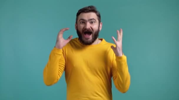 El hombre representa el asombro, muestra el efecto de deleite de la cara. Sorprendido chico feliz emocionado en ropa amarilla. Hermoso modelo chocado masculino sobre fondo azul. — Vídeos de Stock