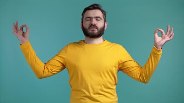 Homem calmo a relaxar, a meditar. Guy se acalma, respira profundamente com mudra om no fundo do estúdio azul. Conceito de ioga. — Vídeo de Stock