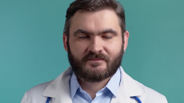Uspokojený lékař v lékařském plášti souhlasně přikyvuje. Pozitivně se usmívající doktor, pojetí řeči těla. Modré pozadí studia. — Stock video