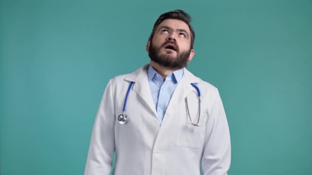 El doctor aburrido suspira y pone los ojos en blanco. Él está en bata blanca sobre fondo de pared azul. Doc está cansado del trabajo, decepcionado, indefenso — Vídeos de Stock