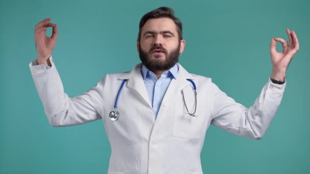 Klidný doktor v bílém lékařském kabátě, relaxující, meditující. Člověk se uklidní, zhluboka se nadechne s mudra om na modrém pozadí studia. — Stock video