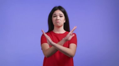 Çapraz el işareti olmadan onaylamayan güzel bir kız Basta, Negatif, bu kadar jest yeter. Reddetmek, reddetmek, anlaşmazlık, menekşe arka planda güzel bir kızın portresi