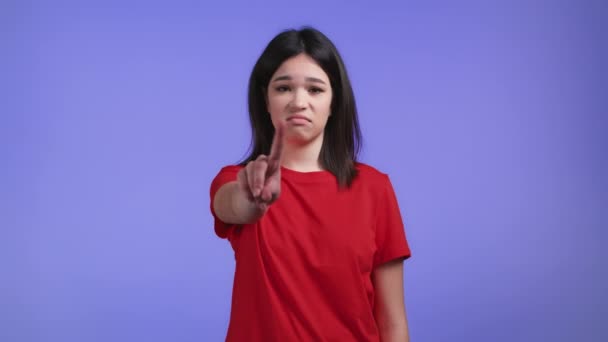Egy komoly nő portréja, amint elutasító gesztust mutat a mutatóujjával. Ne játszadozz velem. Súlyos lány piros pólóban elszigetelt lila háttér. — Stock videók