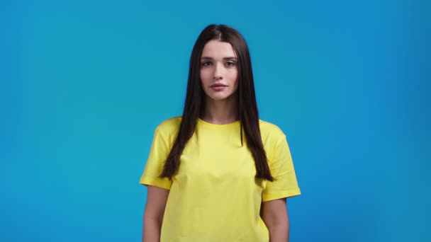 Uma mulher séria a olhar para a câmara. Linda modelo senhora em amarelo t-shirt em azul estúdio fundo. — Vídeo de Stock