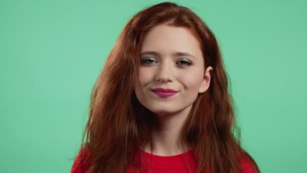 A vörös hajú nő igent mond, bólint a fejével. Fiatal lány narancssárga alapkopásban, testbeszéd koncepció. Zöld stúdió háttér. — Stock videók