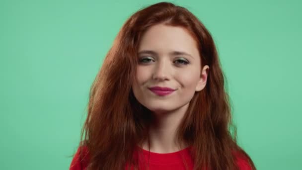 Mujer con el peinado rojo mostrando sí signo, asiente con la cabeza aprobadamente. Chica joven en ropa básica naranja, concepto de lenguaje corporal. Fondo de estudio verde. — Vídeo de stock