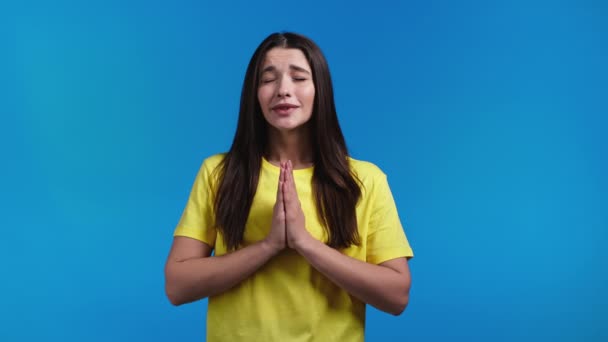 Hübsche Frau betet mit den Händen auf blauem Hintergrund. Mädchen bettelt Gott befriedigen ihre Wünsche, helfen mit. — Stockvideo