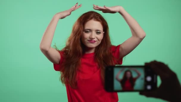 Smiling vlogger woman recording video of herself dancing in front of smartphone camera on green background. Influencer makes funny social media clip — Stock Video