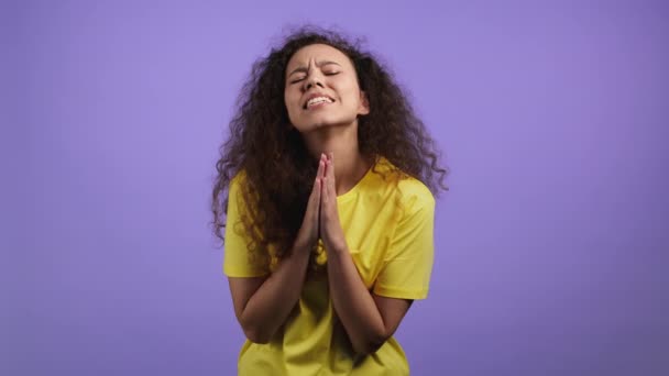 Mujer bonita rezando sobre fondo violeta. Chica con el pelo rizado rogando a Dios para hacer sus sueños realidad, ayudar con. — Vídeos de Stock