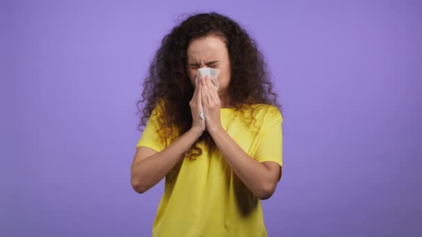 Pretty woman sneezes into tissue. Isolated girl on violet studio background. Lady is sick, has a cold or allergic reaction. Coronavirus, epidemic 2021, illness concept — Stock Video