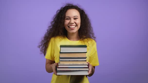 Studentessa tiene pila di libri universitari dalla biblioteca su sfondo viola in studio. Donna sorride, è felice di laurearsi. — Video Stock