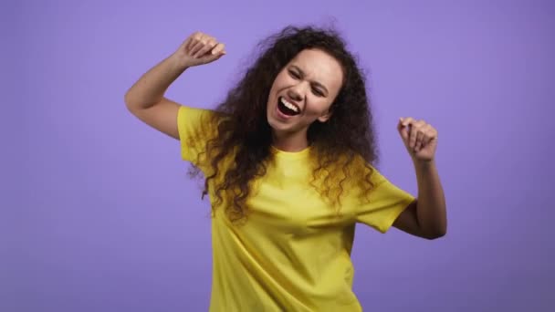 Привлекательная женщина с кудрявой прической танцует на фоне фиолетовой студии. Девушка в желтой одежде. Позитивное настроение. — стоковое видео