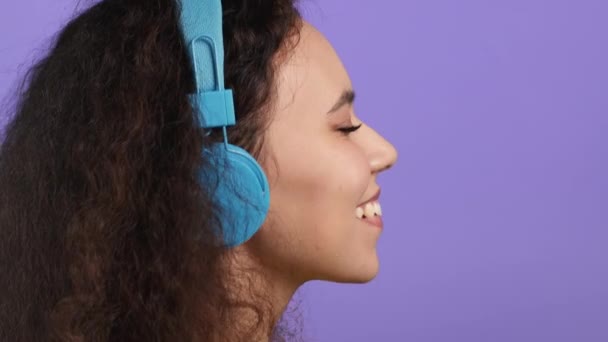 Mujer atractiva con auriculares azules sobre fondo de estudio violeta. Retrato de chicas lindas. Música, radio, felicidad, libertad, concepto de juventud. — Vídeo de stock