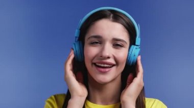 Mavi stüdyo arka planında kablosuz kulaklığı olan çekici bir kadın. Şirin kızlar portresi. Müzik, radyo, mutluluk, özgürlük, gençlik kavramı.