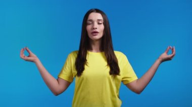 Sakin bir kadın dinleniyor, meditasyon yapıyor. Sakinleşiyor, derin derin derin nefes alıyor. Mavi stüdyo arka planında. Yoga konsepti.