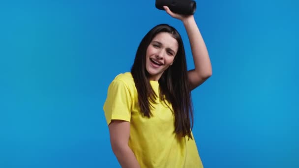 Woman listening to music by wireless portable speaker - modern sound system. Lady dancing, enjoying on blue studio background. She moves to the rhythm of music. — Stock Video