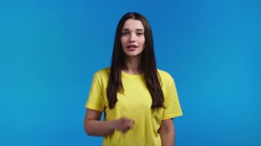 Gülümseyen kadın mavi arka planda parmaklarını tutuyor. Şşş, sır, sessizlik jesti. Kapat.