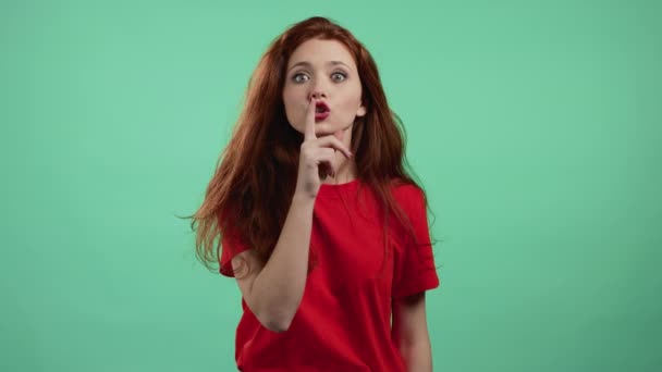 Glimlachende vrouw met rood haar met vinger op haar lippen over groene achtergrond. Het gebaar van de stilte, het geheim. Sluiten. — Stockvideo