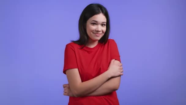 Young modest and shy woman in orange t-shirt looking to camera on violet studio background. — Stock Video