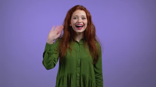 Mujer amigable saludando de la mano - hola, o adiós, chao, adios. Partir, decir adiós a la cámara. Hermosa chica saludando mano sobre fondo de estudio violeta — Vídeos de Stock