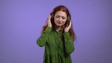 Mor stüdyo arka planında kulaklığı olan güzel bir kadın. Şirin kızlar portresi. Müzik, radyo, mutluluk, dans, gençlik kavramı.