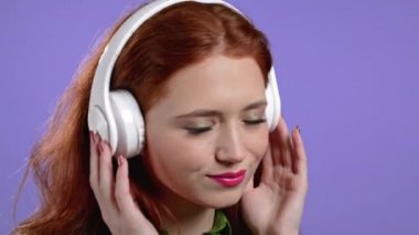 Mor stüdyo arka planında kablosuz kulaklığı olan hoş bir kadın. Şirin kızlar portresi. Müzik, radyo, mutluluk, özgürlük, gençlik kavramı.