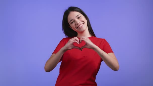 Genre jolie femme faisant signe de forme coeur près de sa poitrine. Fond violet. Santé des femmes, bénévolat, don aide et amour concept. — Video