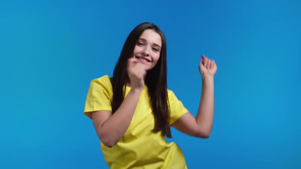 Attraente donna italiana che balla su sfondo blu studio. Ragazza in giallo abbigliamento di base. Umore positivo. Rallentatore. — Video Stock