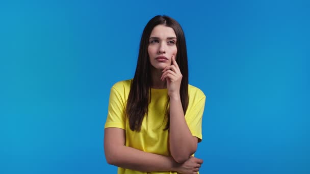 Mujer pensante mirando hacia arriba en el fondo del estudio azul. Expresiones faciales pensativas. Bonita modelo con aspecto atractivo y cabello natural morena. — Vídeo de stock