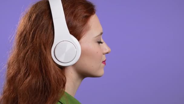 Wanita cantik dengan headphone putih di latar belakang studio ungu. Potret gadis cantik. Musik, radio, kebahagiaan, kebebasan, konsep pemuda. — Stok Video