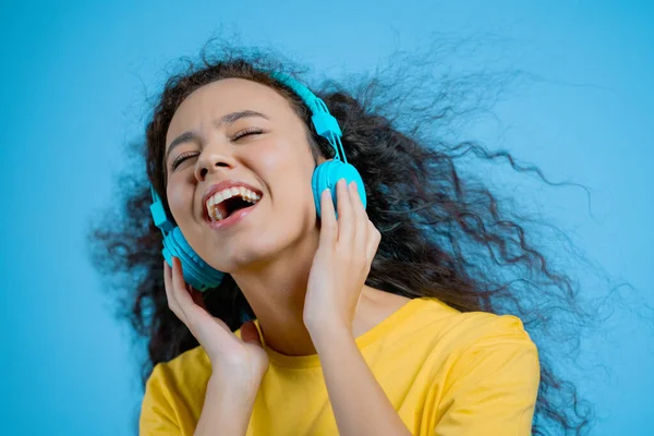 Attraktive Frau, die mit drahtlosen Kopfhörern auf blauem Studiohintergrund tanzt. Nettes Mädchen tanzt und lächelt. Musik, Radio, Glück, Freiheit, Jugendkonzept. — Stockfoto