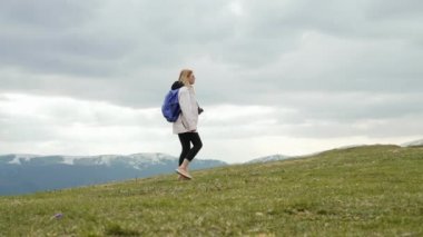 Genç gezgin kadın yüksek dağın tepesinde tek başına yürüyor. Sırt çantalı bayan. Sağlıklı yaşam tarzı, doğa, temiz hava, yolculuk konsepti