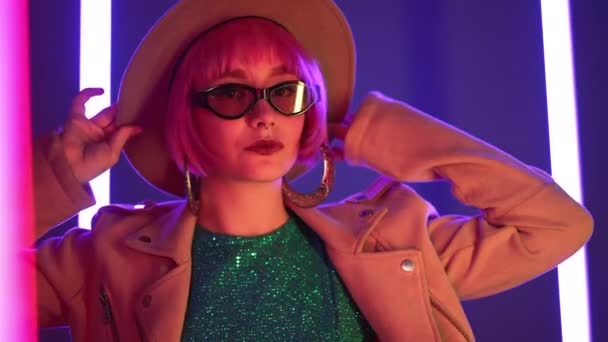 Eccentric woman with pink hair posing near led-colorful neon lamps. Charming odd girl in hat and sunglasses, nightlife concept. Modern model pop outfit, influencer lifestyle. — Stock Footage Eccentric woman with pink hair posing near led-colorful neon lamps. Charming odd girl in hat and sunglasses, nightlife concept. Modern model pop outfit, influencer lifestyle. — Stock Video