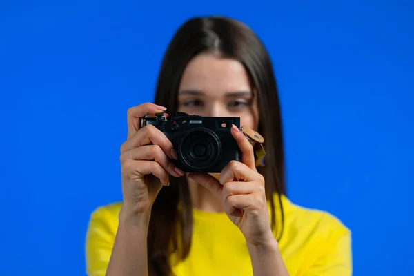 Giovane bella donna scatta foto con fotocamera DSLR su sfondo blu in studio. Ragazza sorridente come fotografo. — Foto Stock