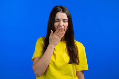 Uykulu kadın esniyor, ağzını eliyle kapatıyor. Çok sıkıcı, ilginç değil. Mavi stüdyo arka planı.