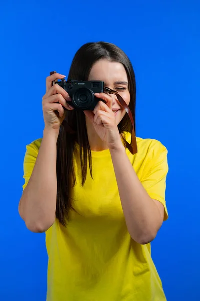 Mladá hezká žena pořizuje snímky s DSLR kamerou nad modrým pozadím ve studiu. Dívka se usmívá jako fotograf. — Stock fotografie