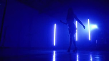 Seksi kıyafetli genç bir kadın, uzun lambalı, mavi stüdyoda müzik eşliğinde dans ediyor. Bayan tek başına gösteri yapıyor. Cinsel dans, koreografi, sanat kavramı