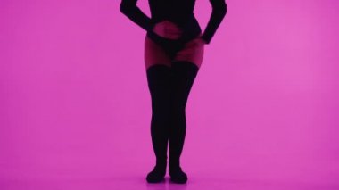 Esnek seksi dansçıların çoraplı bacakları. Tanımlanamayan bir kadın pembe arka planda, parlak bir ışıkla dans ediyor. Güzel ince kadın vücudu..