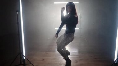Dumanlı odada güzel ve baştan çıkarıcı bir şekilde dans eden kadın dansçı. Yüksek topuklu bir kadın vücut ve saçlarıyla egzersiz yapıyor. Yavaş çekim