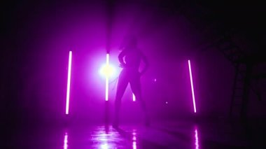 Genç bayan, koyu mor stüdyoda tek başına dans edip seksi dans ediyor. Bayan vücudunu ve saçlarını müzik ritmine göre hareket ettiriyor. Yavaş çekim.