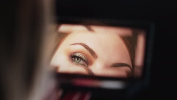Reflection in mirror of womans eyes with shinning make-up. Young lady looks at herself. Makeup at night getting ready before going to party. Slow motion — Stock Video