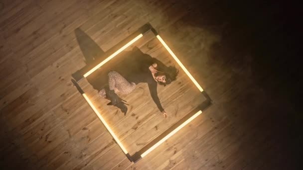 Sexy žena provádí pružné pohyby se svým tělem ležícím na podlaze. Svůdný tanec ve studiu mezi lampami. Dámská tanečnice v těsných šatech a podpatcích. Horní pohled. — Stock video