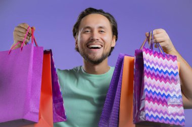 Yakışıklı adam menekşe stüdyosunun arka planında alışveriş poşetleri tutuyor. Adam indirimli satışlardan hediyeler aldı..