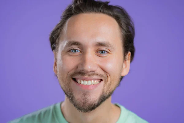 Portrét usměvavého Evropana. Mladý pohledný chlap s vousem na fialové pozadí studia. — Stock fotografie