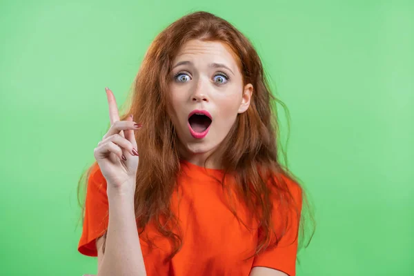 Porträt einer jungen Frau, die eine Idee hat und mit erhobenem Finger auf grünem Studiohintergrund zeigt. Lächelndes glückliches Mädchen zeigt Eureka-Geste. — Stockfoto