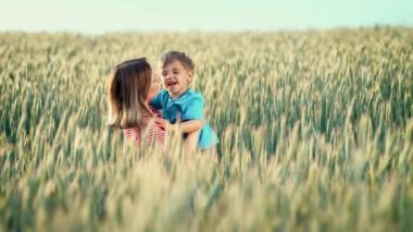 Anne ve çocuğunun taze buğday tarlasında güzel bir sahnesi. Mutlu anne ve oğlan kucaklaşıyor, gülümsüyor. Aile, aşk, çocukluk kavramı.