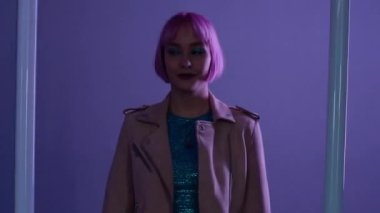 Pembe saçlı, kurşunlu neon lambaların yanında poz veren tuhaf bir kadın. Çekici bir kız, gece hayatı konsepti. Modern model pop kıyafeti, etkileyici yaşam tarzı..