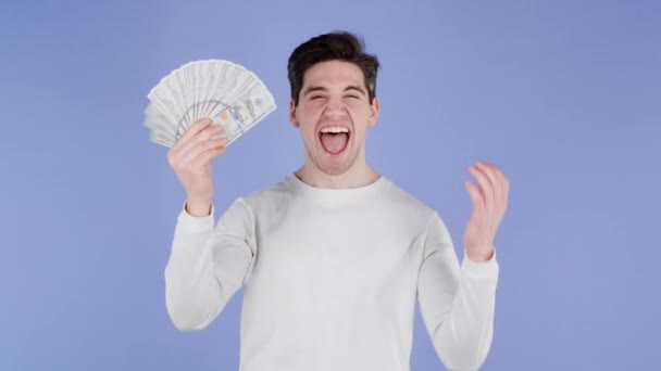 Szczęśliwy podekscytowany człowiek z pieniędzmi gotówkowymi - dolary amerykańskie banknoty na fioletowej ścianie. Symbol jackpota, zysk, zwycięstwo, wygrana na loterii — Wideo stockowe