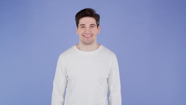Porträtt av leende glad stilig man i vit klädsel tittar på kameran. Guy i studio på ljus violett bakgrund. — Stockvideo